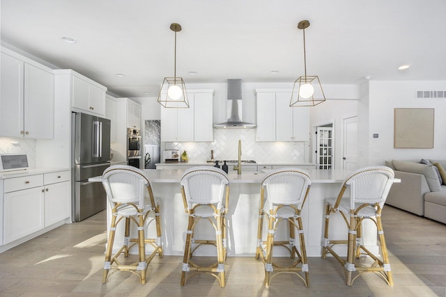 kitchen with white cabinetry, hanging light fixtures, stainless steel appliances, and wall chimney exhaust hood