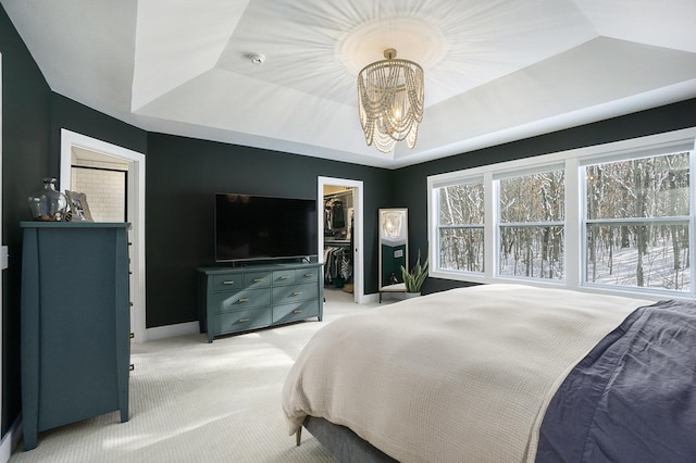 carpeted bedroom featuring a raised ceiling, a walk in closet, an inviting chandelier, and a closet