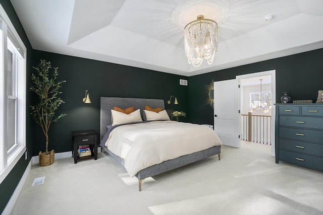 bedroom with an inviting chandelier, a tray ceiling, and light carpet