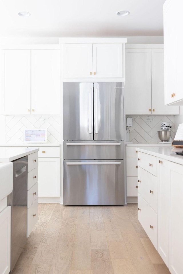 kitchen with appliances with stainless steel finishes, light wood-type flooring, white cabinets, and backsplash