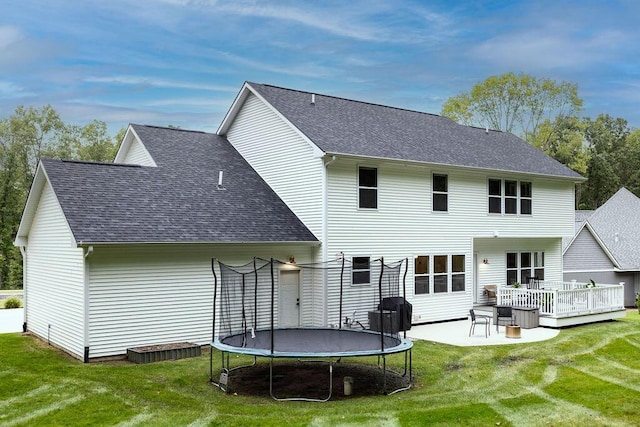 rear view of property featuring a trampoline, a wooden deck, and a lawn