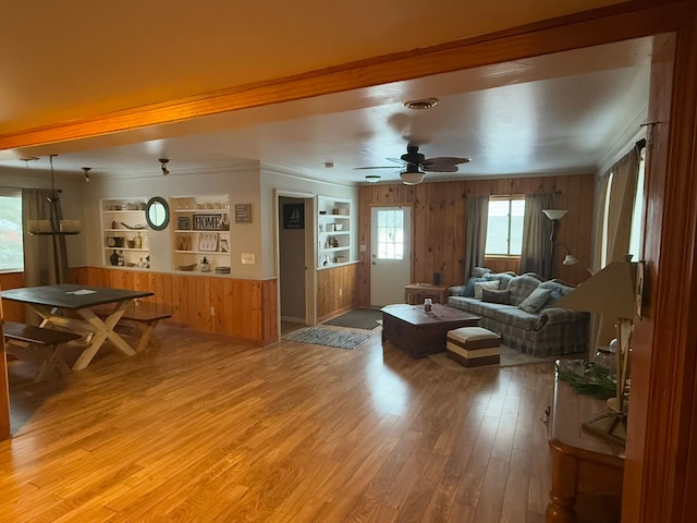 living room with built in features, ceiling fan, ornamental molding, light hardwood / wood-style floors, and wood walls