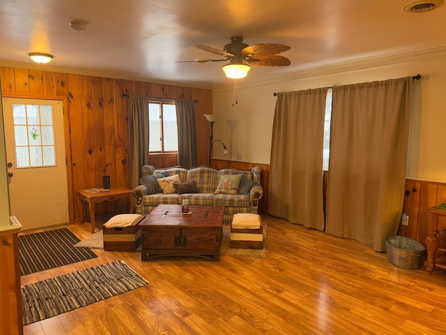 living room with ornamental molding, ceiling fan, wooden walls, and light hardwood / wood-style flooring