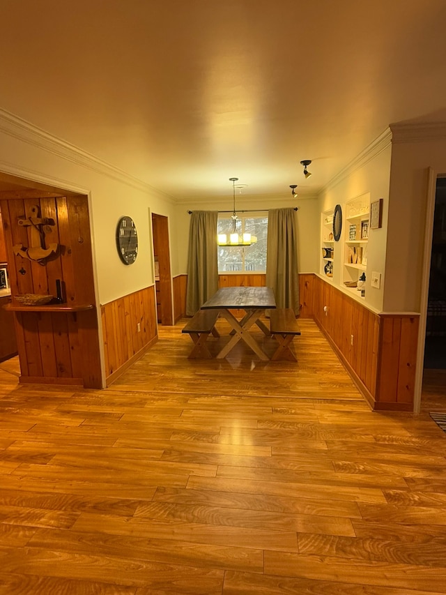 dining area featuring crown molding, a notable chandelier, wood walls, and light wood-type flooring