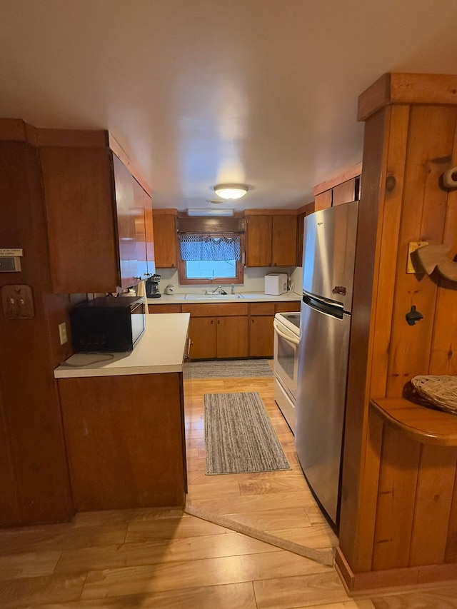 kitchen with stainless steel refrigerator, white electric stove, sink, and light wood-type flooring