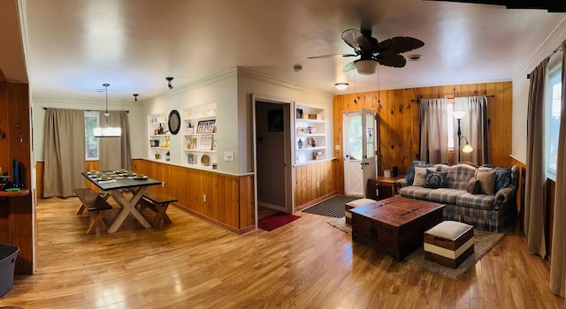 living room with crown molding, built in features, light hardwood / wood-style flooring, and wood walls