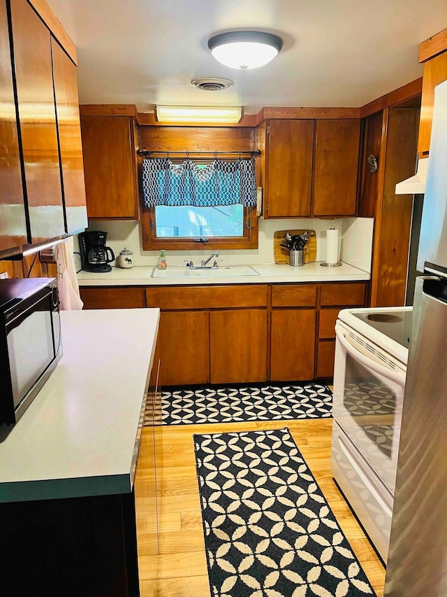 kitchen with stainless steel refrigerator, white electric range, sink, and light hardwood / wood-style flooring