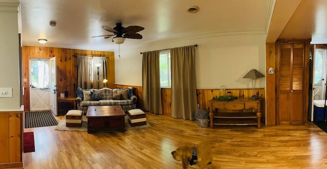 living area with crown molding, wood walls, ceiling fan, and light wood-type flooring