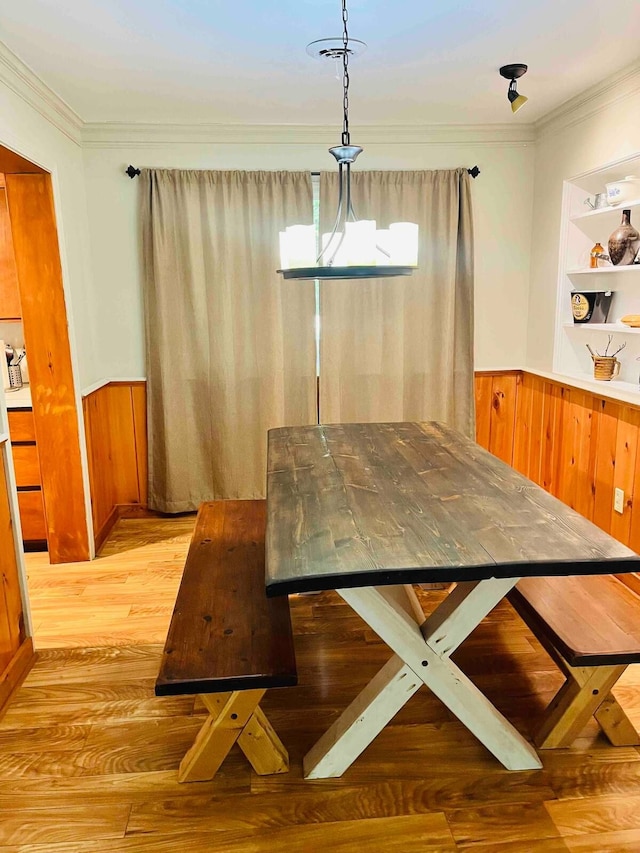 dining room featuring crown molding, wooden walls, and light hardwood / wood-style flooring