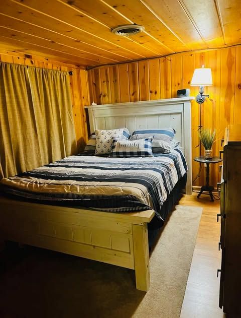 bedroom with wood ceiling, wooden walls, and light wood-type flooring