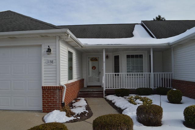 snow covered property entrance with a garage and covered porch