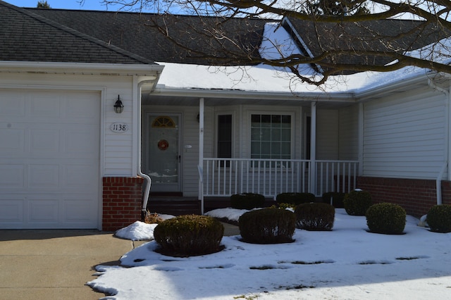 snow covered property entrance with a garage and a porch