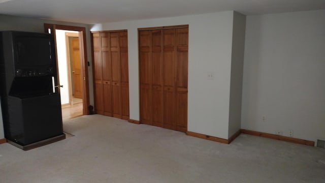 unfurnished bedroom with multiple closets, light colored carpet, and washer / dryer