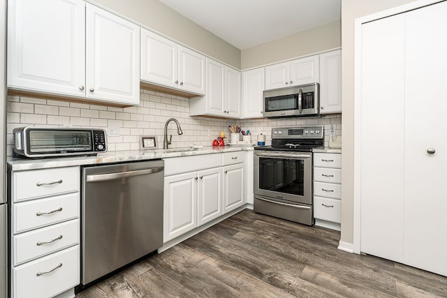 kitchen with appliances with stainless steel finishes, dark hardwood / wood-style floors, tasteful backsplash, white cabinetry, and sink