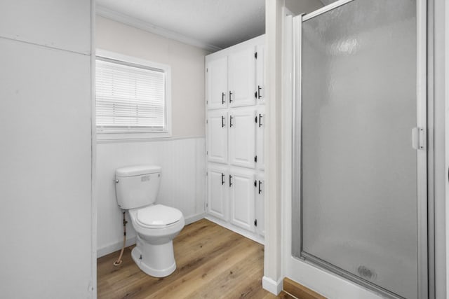 bathroom featuring a shower with door, wood-type flooring, ornamental molding, and toilet