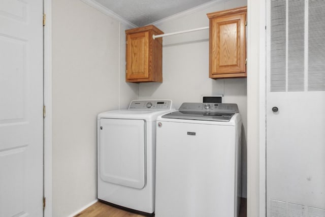 laundry room with crown molding, cabinets, a textured ceiling, light wood-type flooring, and washing machine and dryer