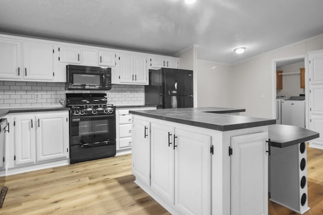 kitchen featuring white cabinetry, black appliances, washing machine and clothes dryer, a kitchen island, and light wood-type flooring