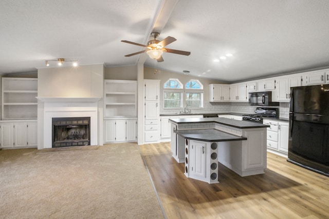 kitchen with vaulted ceiling with beams, white cabinetry, black appliances, a center island, and backsplash