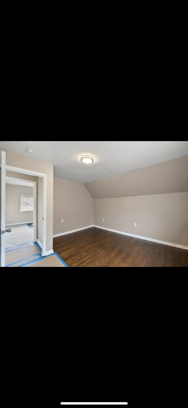 spare room with dark hardwood / wood-style flooring and vaulted ceiling