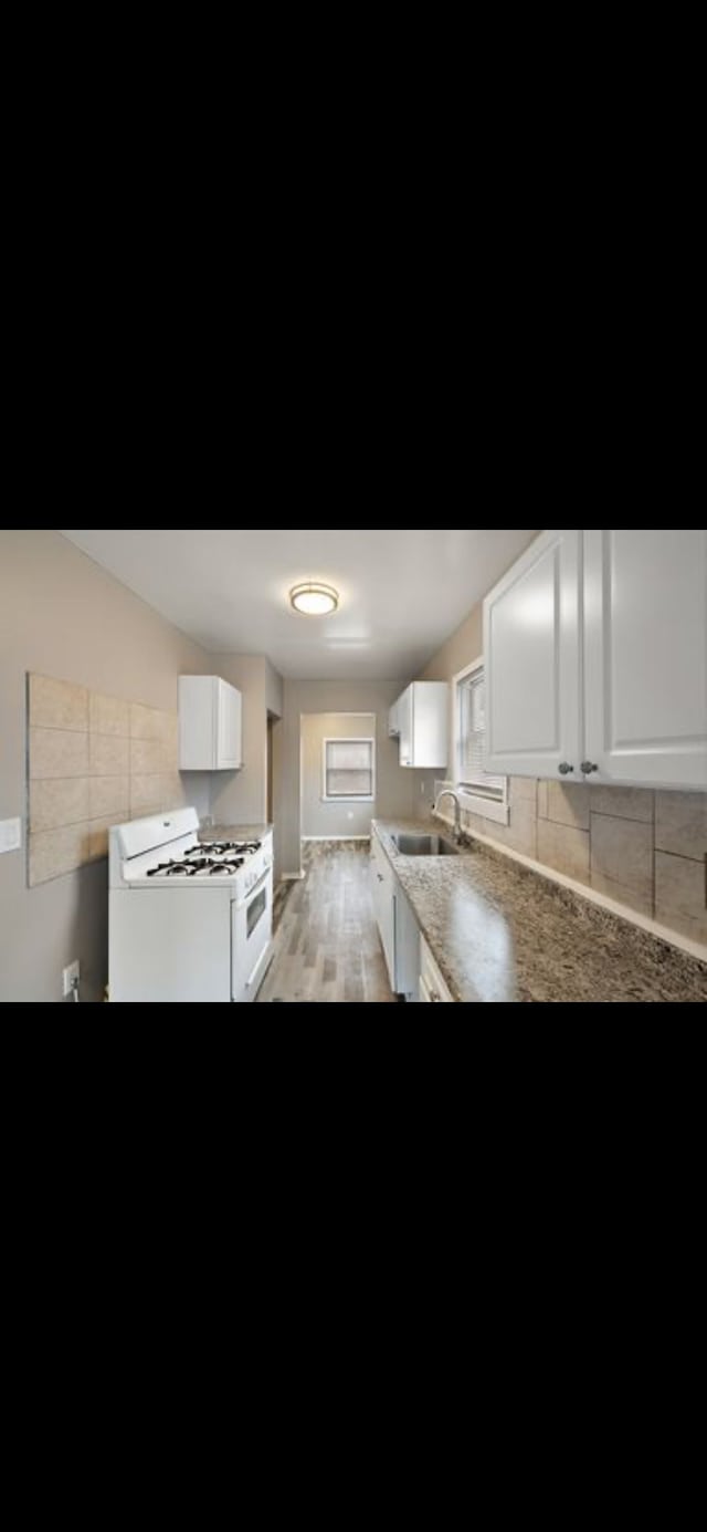 kitchen featuring sink, gas range gas stove, light hardwood / wood-style floors, decorative backsplash, and white cabinets