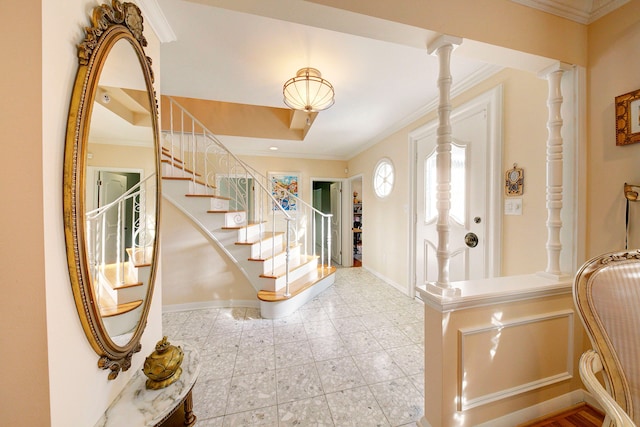 foyer featuring crown molding, a raised ceiling, and decorative columns