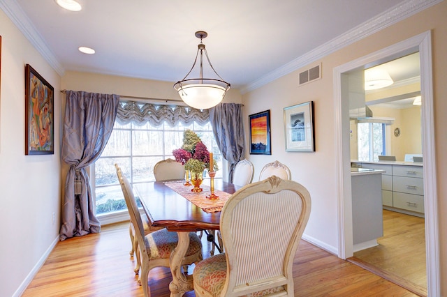 dining space with ornamental molding and light hardwood / wood-style flooring