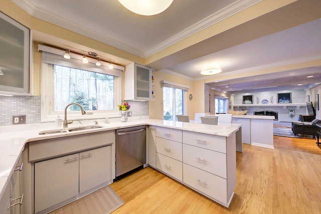 kitchen featuring sink, ornamental molding, stainless steel dishwasher, kitchen peninsula, and light wood-type flooring