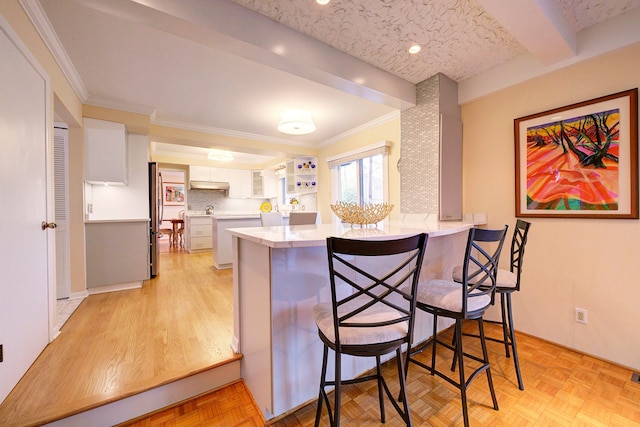 kitchen with stainless steel refrigerator, white cabinetry, a kitchen bar, kitchen peninsula, and light parquet flooring