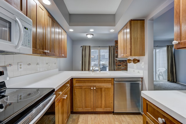 kitchen with appliances with stainless steel finishes, sink, backsplash, and light wood-type flooring