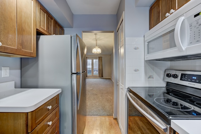 kitchen featuring appliances with stainless steel finishes, pendant lighting, backsplash, and light carpet