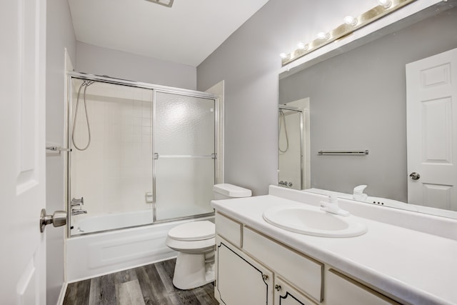 full bathroom featuring hardwood / wood-style flooring, vanity, shower / bath combination with glass door, and toilet