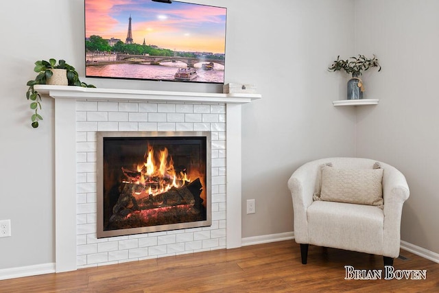 sitting room with a brick fireplace and wood-type flooring