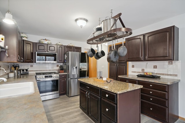 kitchen featuring sink, light hardwood / wood-style flooring, dark brown cabinets, stainless steel appliances, and decorative light fixtures