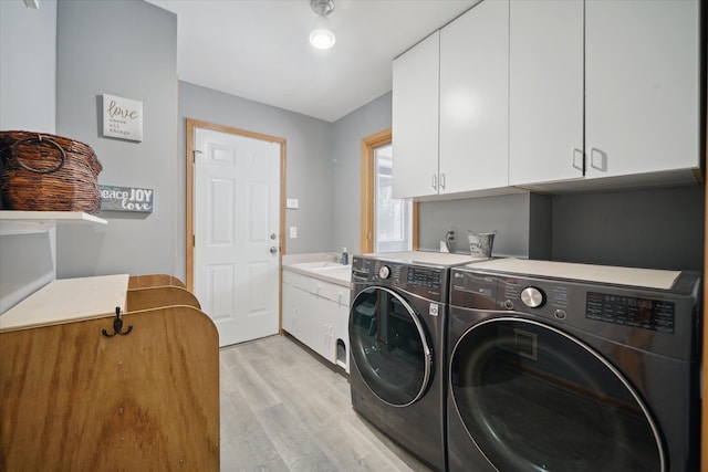 clothes washing area with sink, washer and clothes dryer, cabinets, and light wood-type flooring