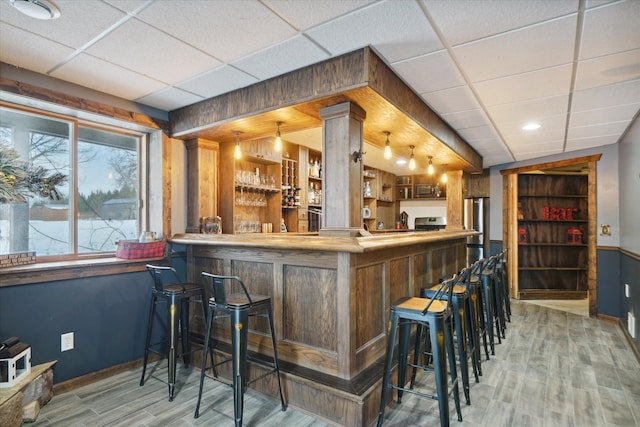 bar with hanging light fixtures, appliances with stainless steel finishes, hardwood / wood-style floors, and a drop ceiling