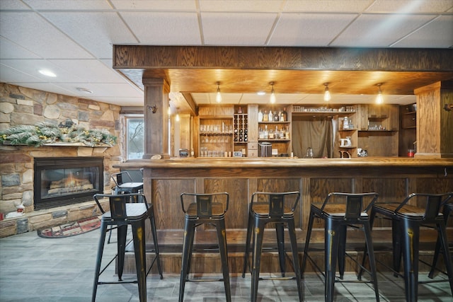 bar featuring a paneled ceiling and a stone fireplace