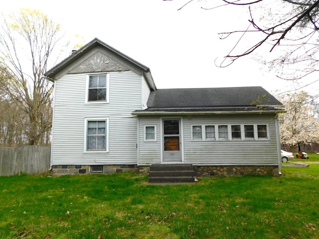 rear view of house featuring fence, a lawn, entry steps, and roof with shingles