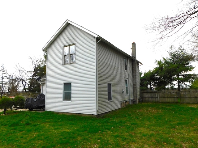 view of side of property with a lawn, a chimney, and fence