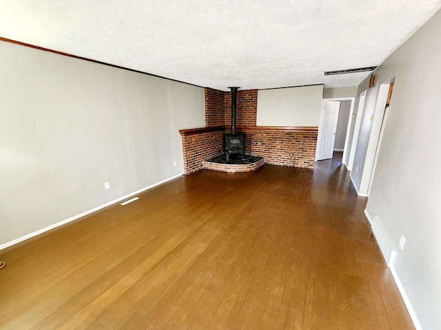 unfurnished living room with wood-type flooring, a textured ceiling, and a wood stove