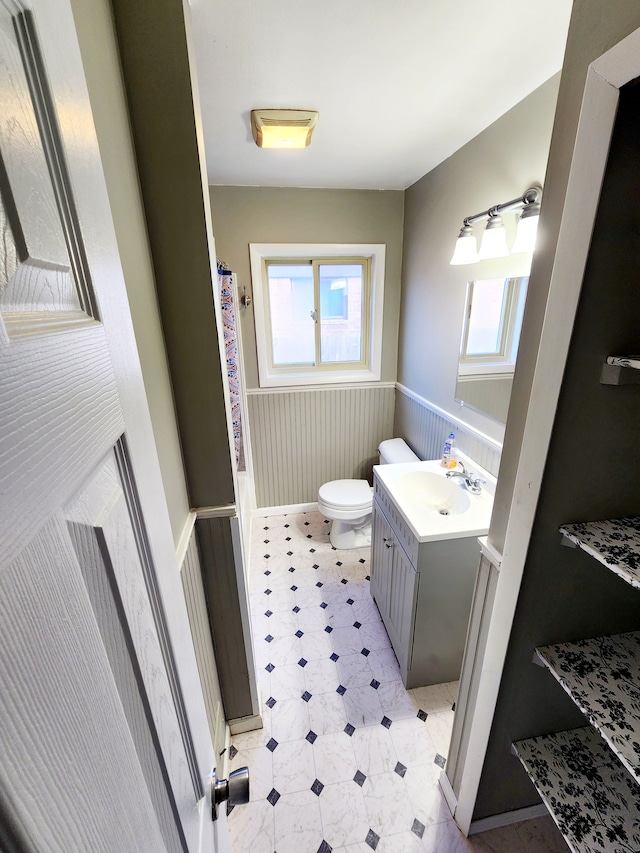 bathroom featuring a wainscoted wall, toilet, a shower with shower curtain, tile patterned floors, and vanity