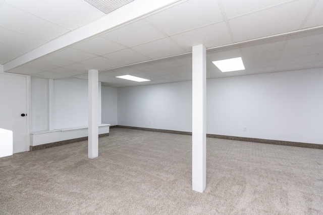 basement featuring a paneled ceiling and light colored carpet