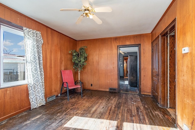 unfurnished room featuring dark wood-type flooring, ceiling fan, ornamental molding, and wood walls