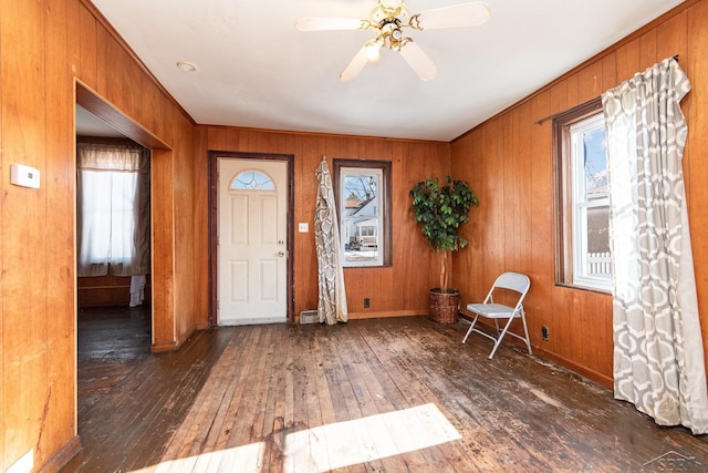 entryway featuring a healthy amount of sunlight, dark hardwood / wood-style floors, wooden walls, and ceiling fan