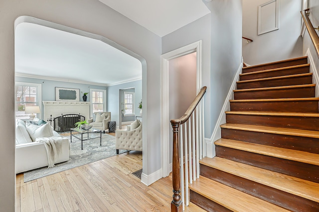 staircase with crown molding, hardwood / wood-style flooring, a fireplace, and a wealth of natural light