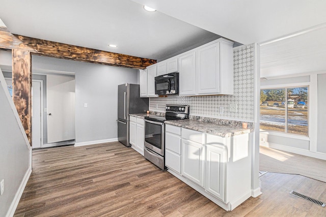 kitchen with decorative backsplash, appliances with stainless steel finishes, white cabinets, and light hardwood / wood-style flooring