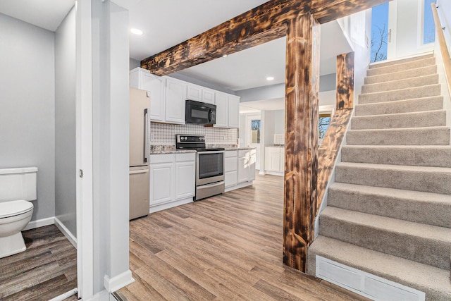 kitchen featuring white cabinets, decorative backsplash, stainless steel appliances, beam ceiling, and light hardwood / wood-style flooring