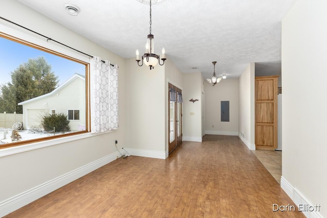 empty room featuring a notable chandelier, light hardwood / wood-style flooring, electric panel, and a textured ceiling