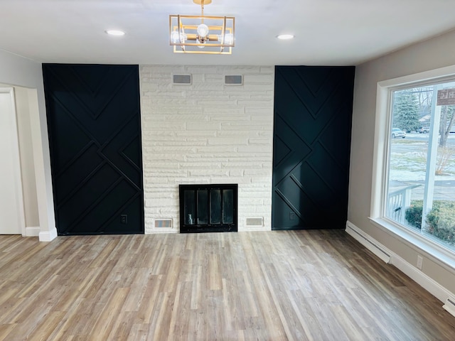 unfurnished living room featuring baseboard heating, plenty of natural light, a stone fireplace, and wood-type flooring