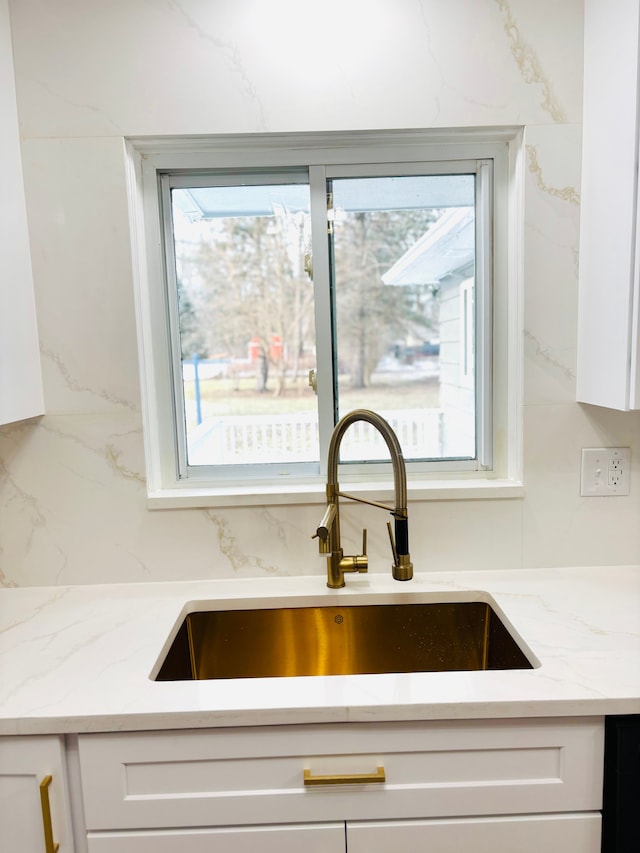 interior details featuring white cabinetry, light stone countertops, and a sink