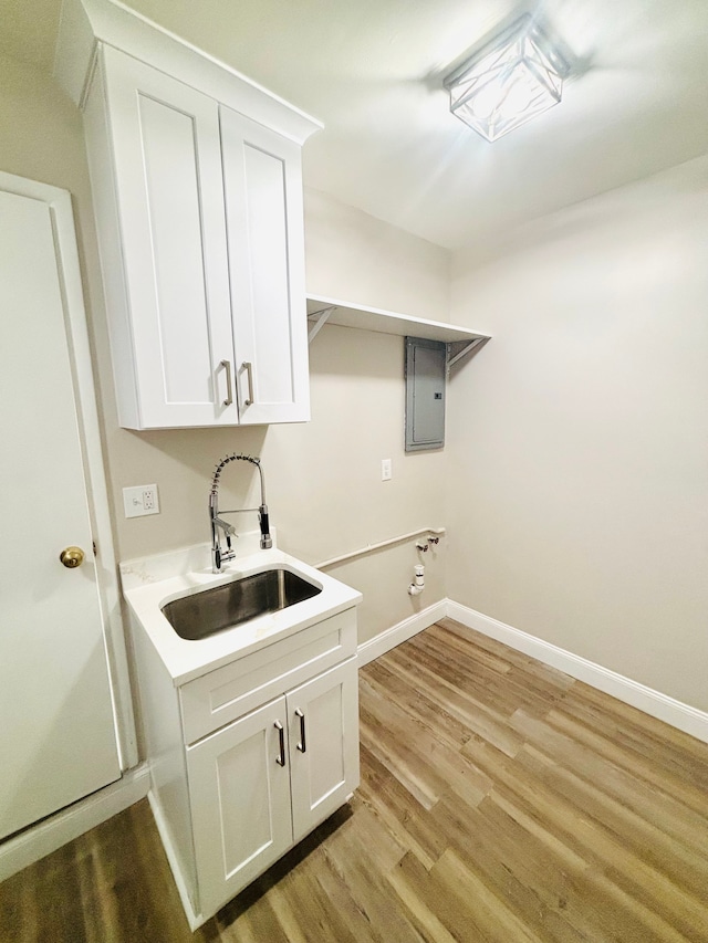 washroom featuring baseboards, light wood finished floors, electric panel, cabinet space, and a sink